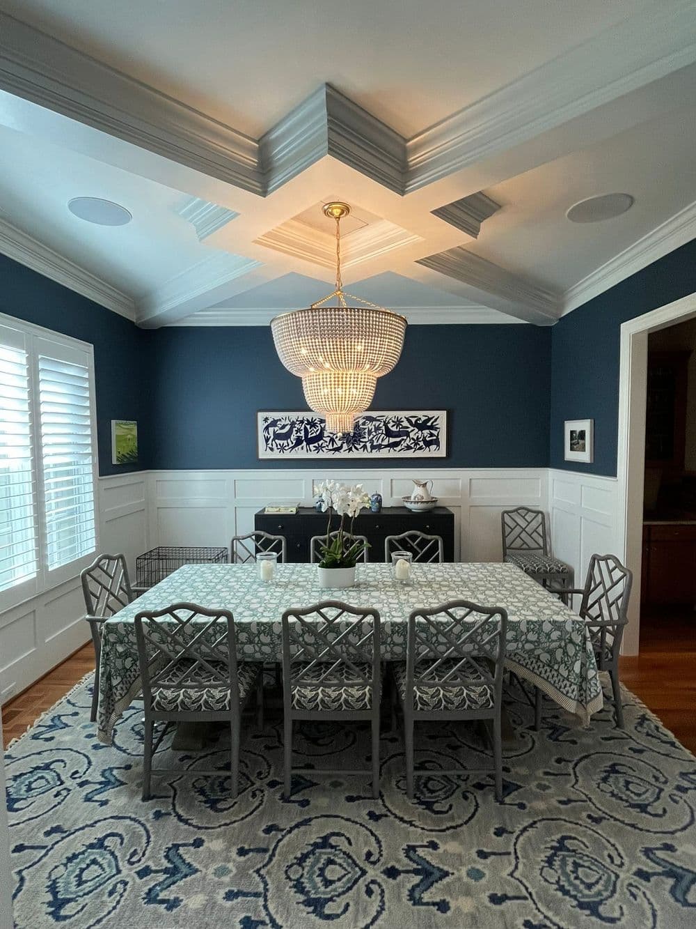 Elegant dining room featuring a chandelier, blue walls, and a patterned tablecloth.