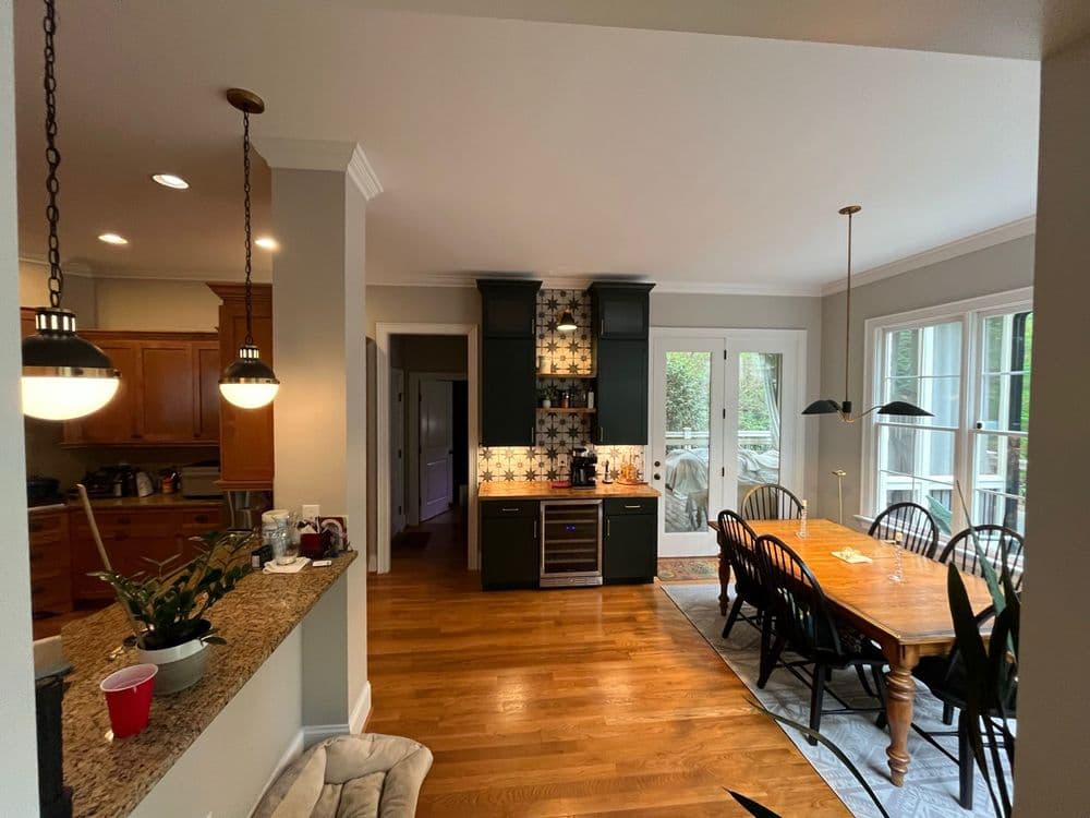 Open kitchen with wooden cabinets, dining area, and natural light from large windows.