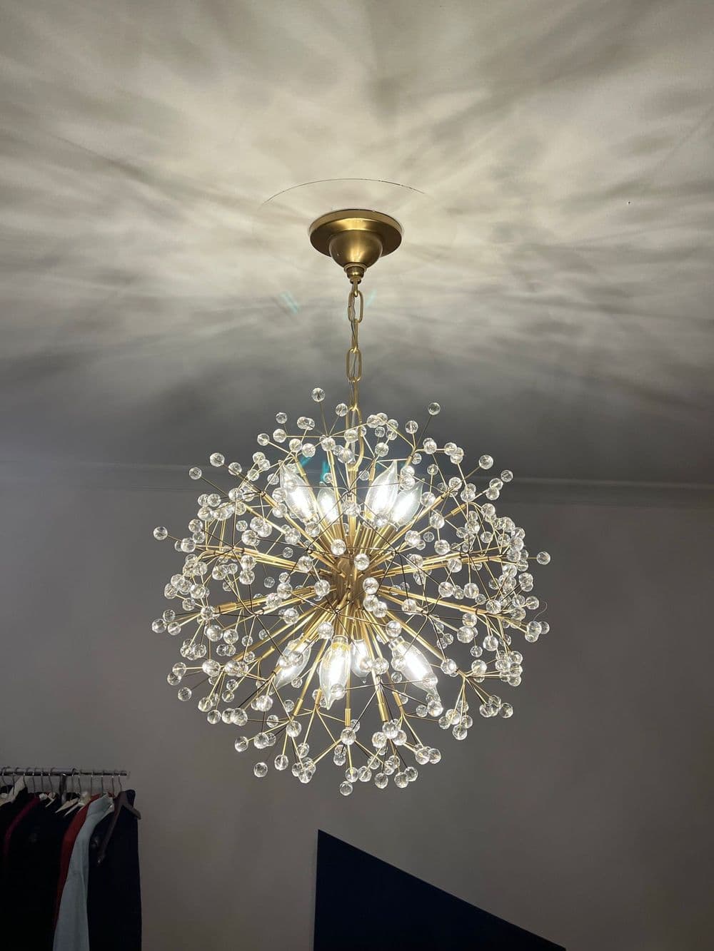 Modern gold chandelier with crystal accents casting decorative shadows on the ceiling.