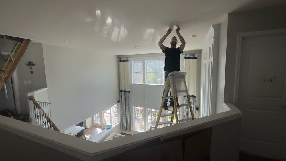 Person on ladder changing ceiling light fixture in bright, modern home interior.