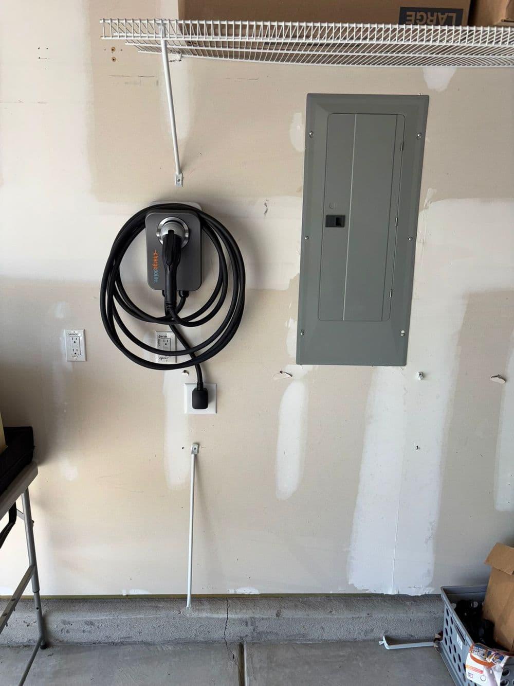 Electric vehicle charging station mounted on garage wall next to electrical panel.