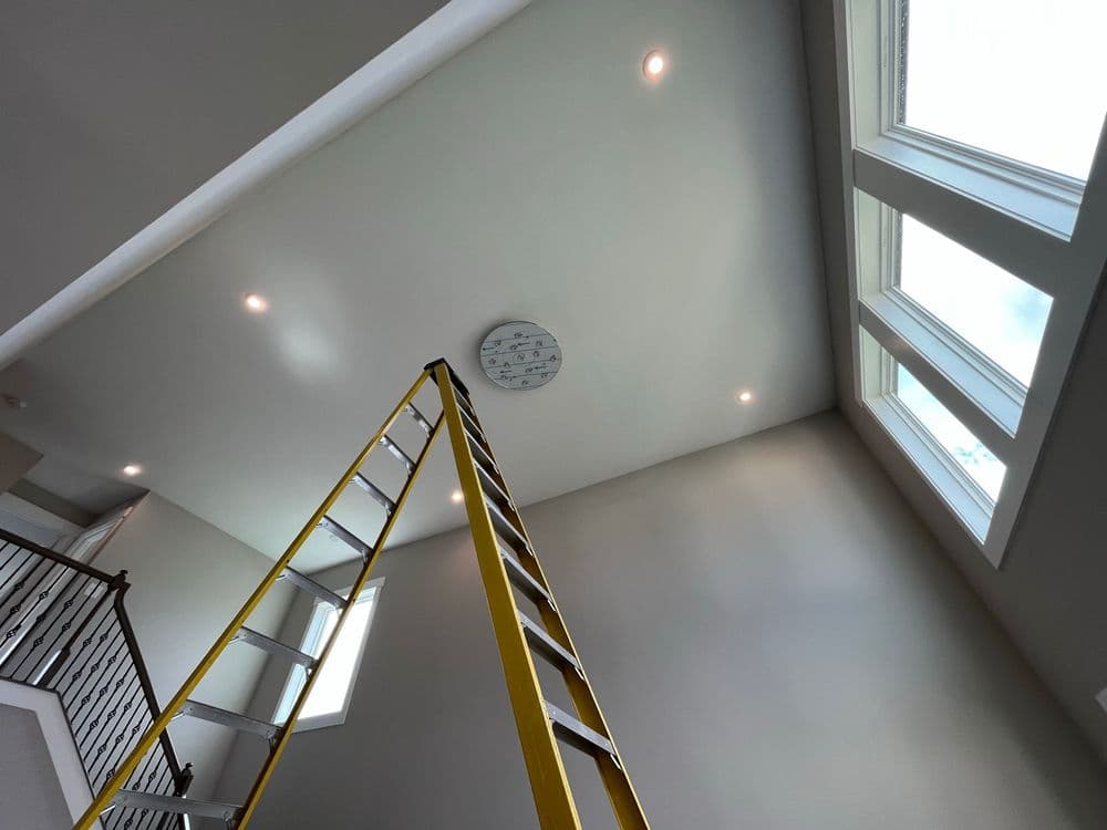 Ladder positioned towards modern ceiling with recessed lights and large windows.