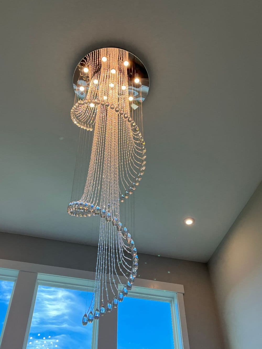 Modern chandelier with cascading crystal beads, bright lighting, and a sleek design.