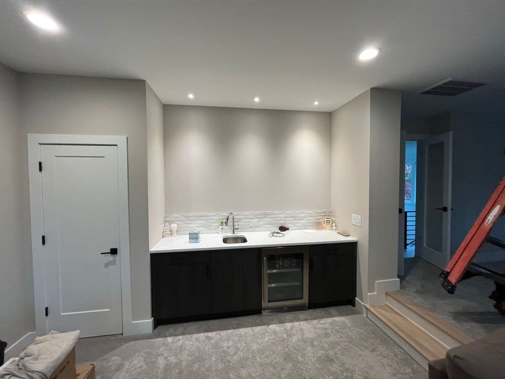 Modern kitchenette with dark cabinetry, white countertop, and subtle lighting in a contemporary space.