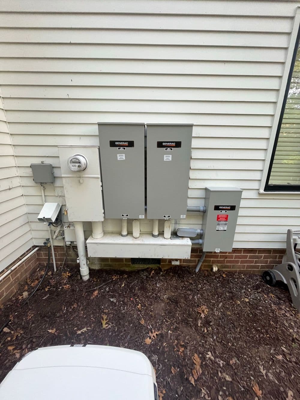 Electrical meter and utility boxes mounted on a house exterior wall, with pipes below.