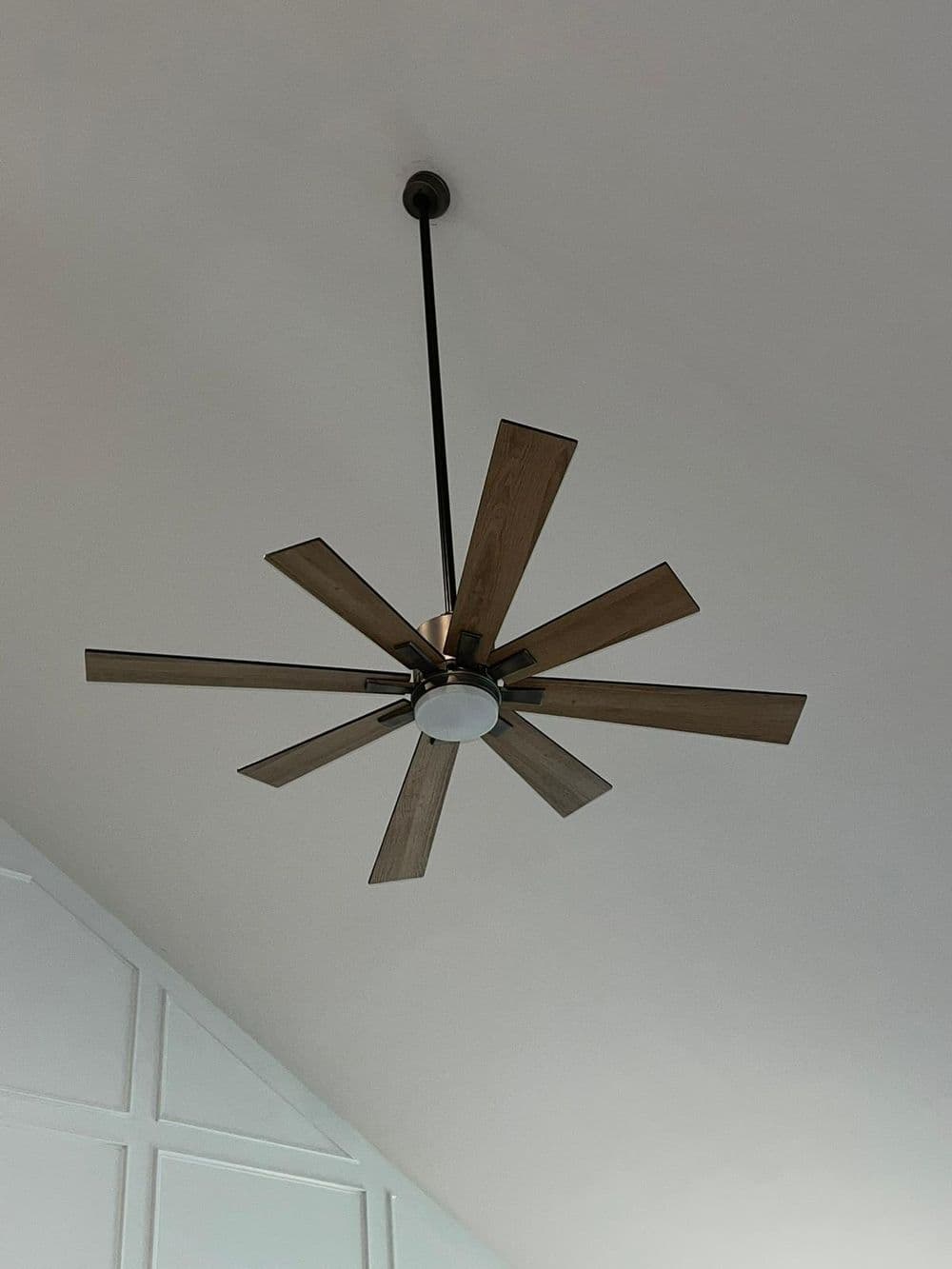 Ceiling fan with wooden blades and light fixture, suspended from a high ceiling.