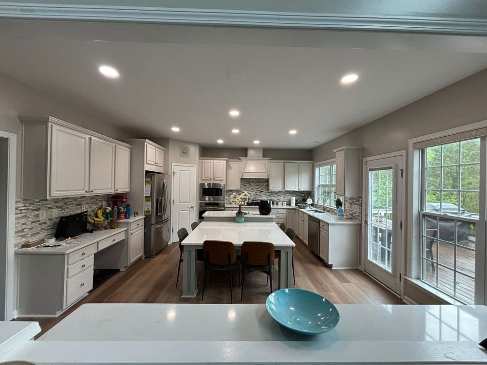 Modern kitchen with white cabinets, large island, and gray backsplash, featuring natural light.
