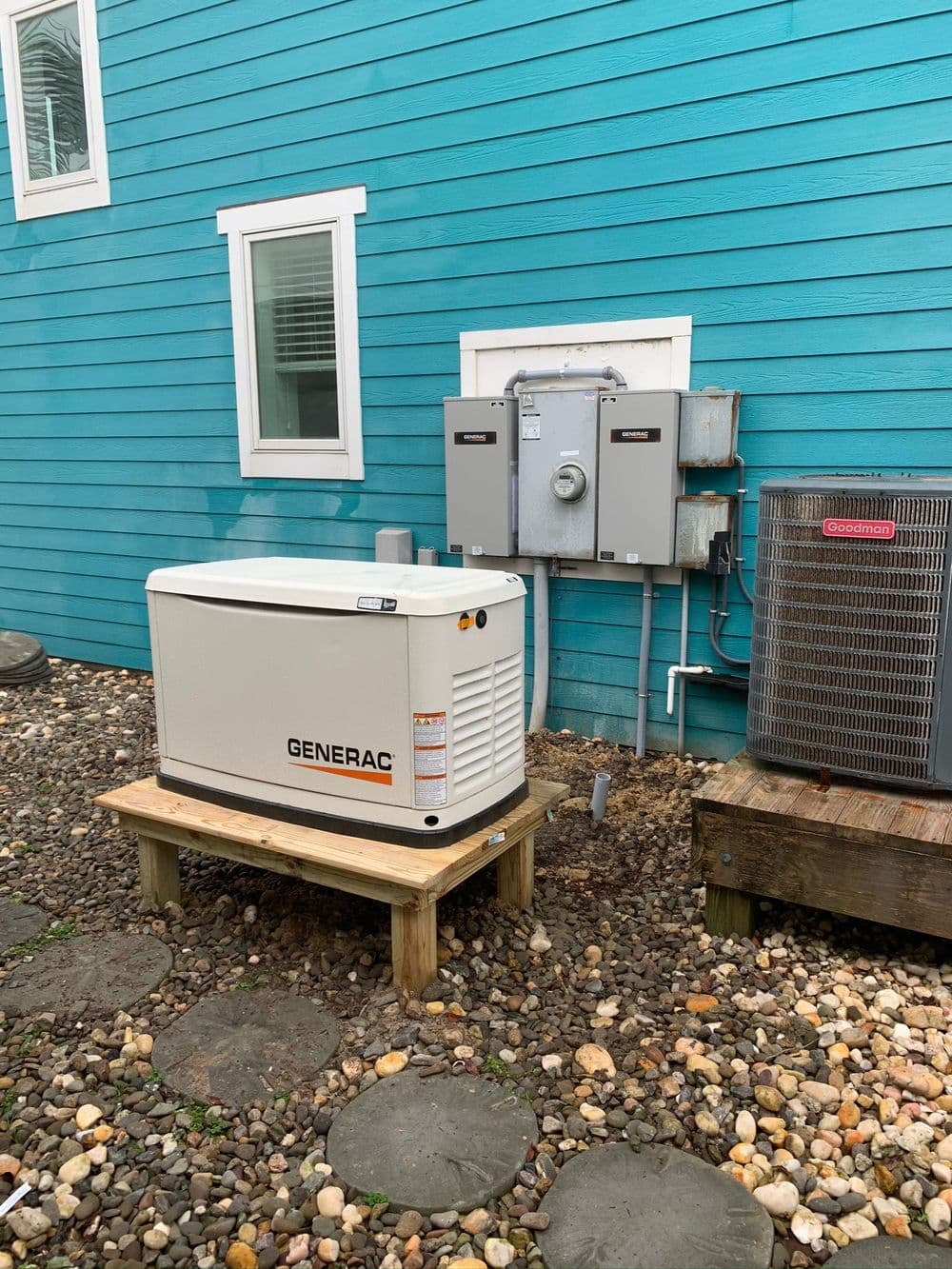 Generac generator installed outside a turquoise house with electrical panel nearby.