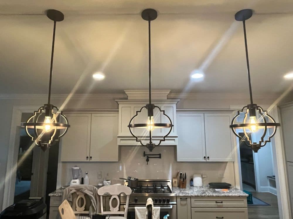 Modern kitchen with three ornate pendant lights and stainless steel appliances.