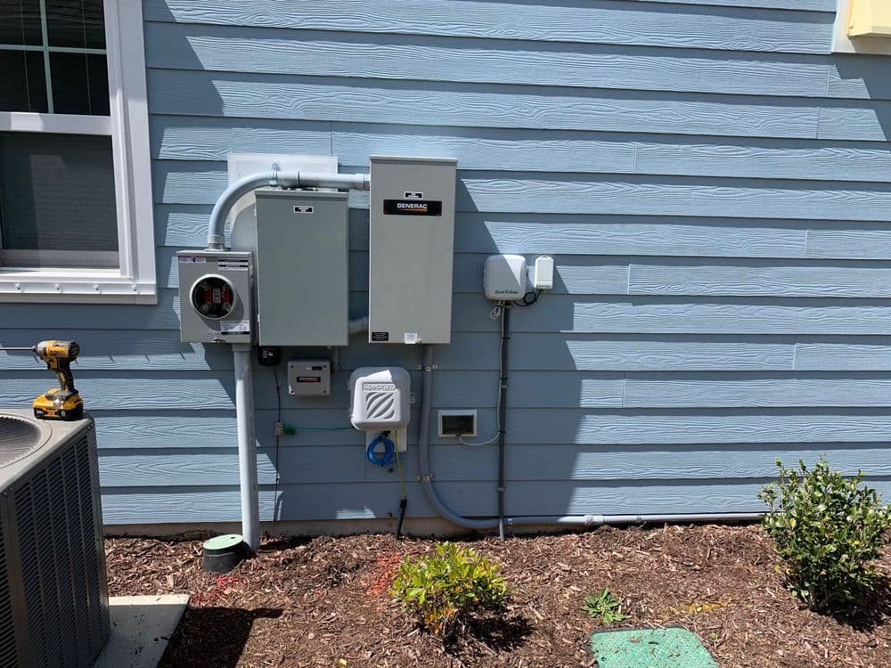 Electrical meter and service panel mounted on a blue house exterior with surrounding landscaping.