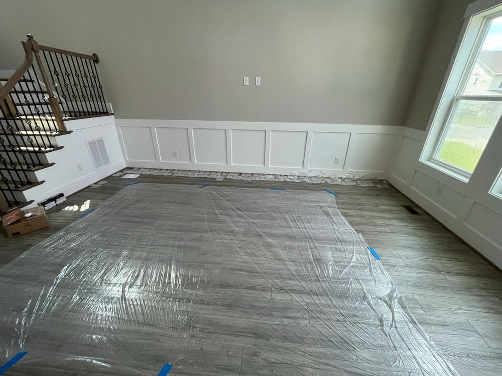 Living room undergoing renovation with protective plastic covering the floor and unfinished walls.