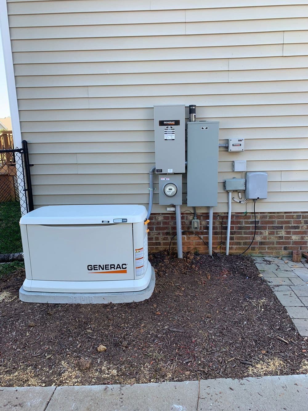 Generac home generator installation beside electrical panel on exterior wall.
