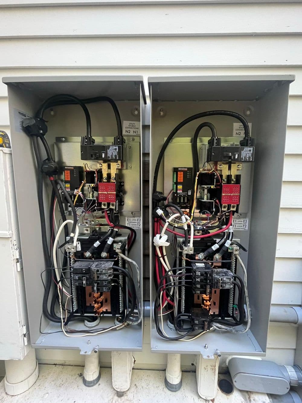 Electrical service panel with circuit breakers and wiring, mounted on a house exterior.