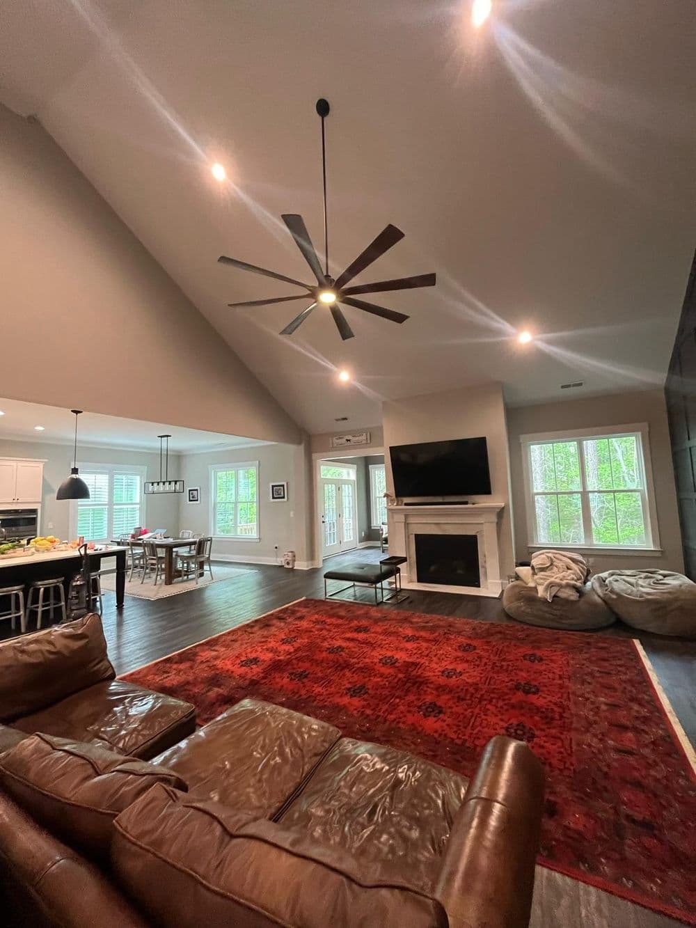 Spacious modern living room with ceiling fan, fireplace, and large windows overlooking nature.