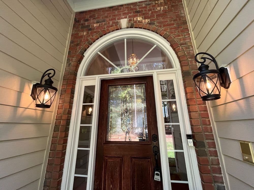 Front entrance with wooden door, arched window, and lanterns on brick wall.