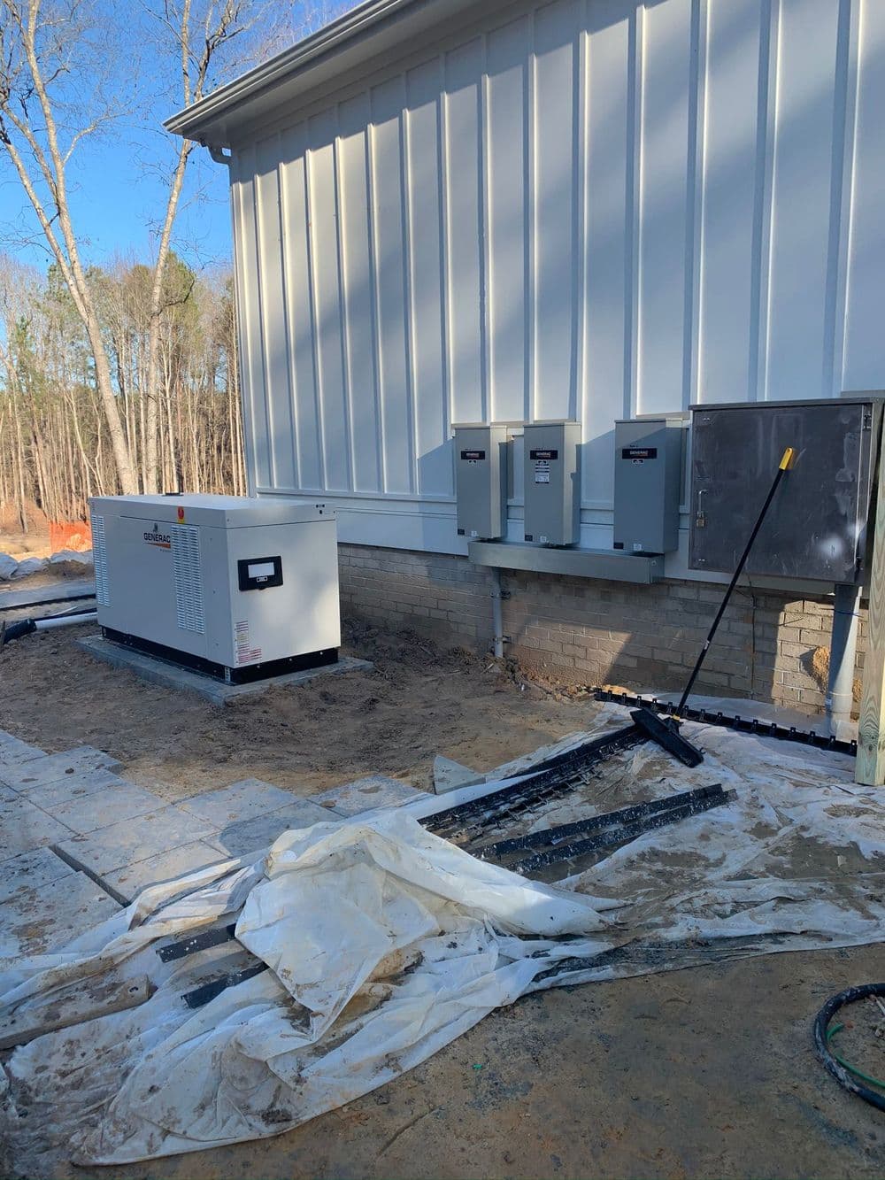 Generator installation beside a new building with electrical panels and construction materials.