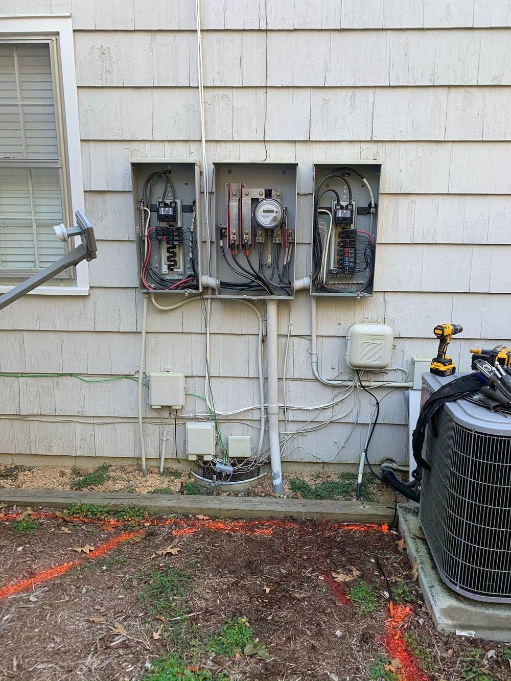 Electrical panel installation with multiple circuits and meter on exterior wall of home.
