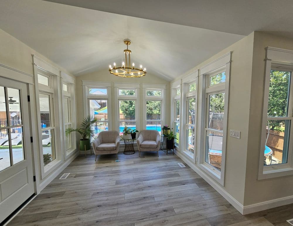 Bright sunroom with large windows, comfy chairs, and a view of the pool outside.