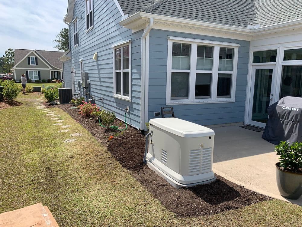 Generator installation beside a blue house with landscaped garden and outdoor furniture.