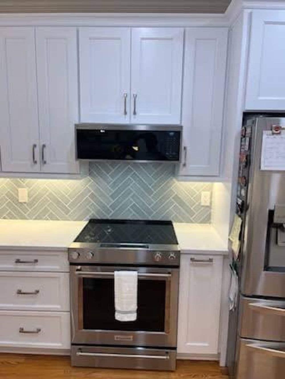 Modern kitchen with stainless steel stove, hood, and white cabinetry featuring herringbone backsplash.