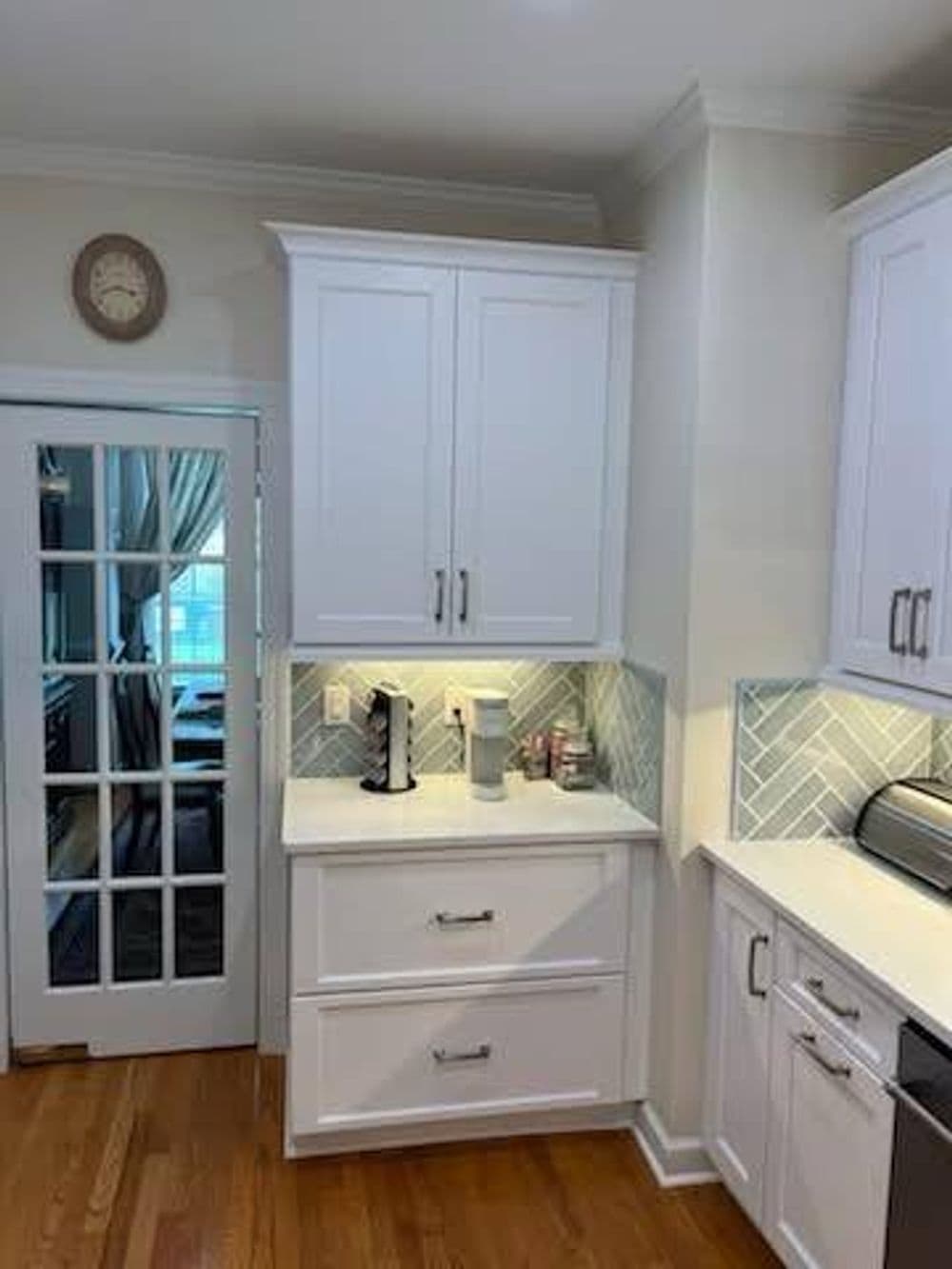 Modern kitchen with white cabinetry, herringbone backsplash, and stylish clock on the wall.
