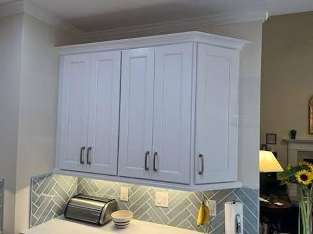 Modern kitchen cabinets with sleek white finish and herringbone backsplash. Stylish storage solution.