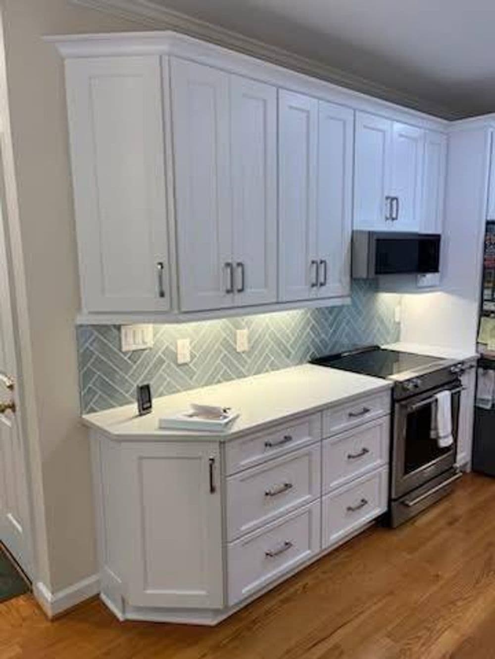 Modern kitchen with white cabinets, herringbone backsplash, and stainless steel appliances.