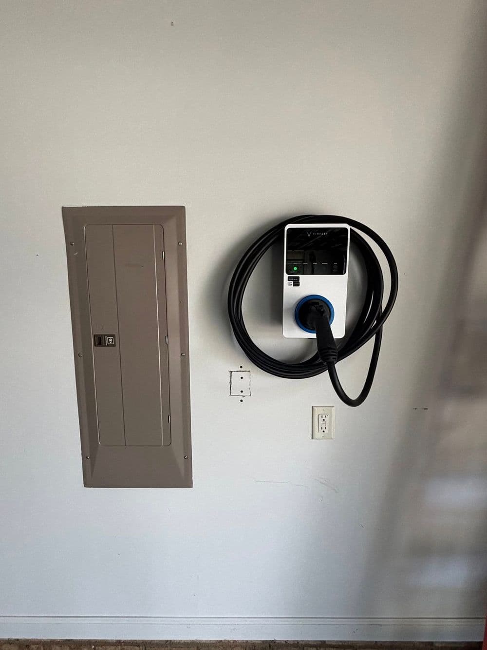 Electric vehicle charger mounted on a wall next to a circuit breaker panel.