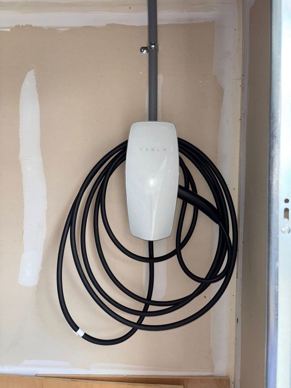 Tesla wall connector with charging cable installed on a wall, ideal for electric vehicle charging.